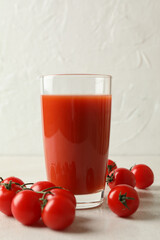 Glass of tomato juice and tomatoes on white textured background