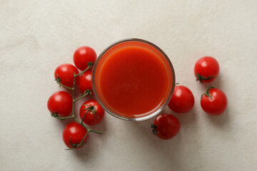 Glass of tomato juice and tomatoes on white textured background