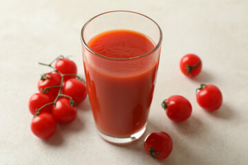 Glass of tomato juice and tomatoes on white textured background