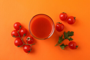 Glass of tomato juice and tomatoes on orange background