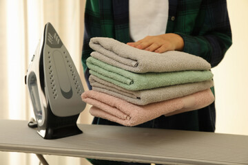 Woman hold pile of towels over ironing board with iron