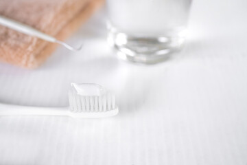 Fototapeta na wymiar White toothpaste on toothbrush with blur image of towel water in glass on white floor background. oral hygiene equipment and dental health care concept.