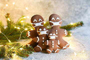 Gingerbread family in a mask. Christmas background. Gingerbread, spruce and lights. Quarantine.