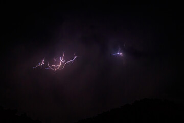 Lightning discharges in the stormy sky under dark rain clouds at night