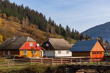 Obraz premium A small village located in a mountain valley. Autumn mountain landscape in the Ukrainian Carpathians - yellow and red trees combined with green needles.