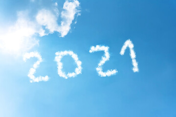 Numbers 2021 symbol inscription on a background of blue sky from white smoke of clouds lit by a bright sun.