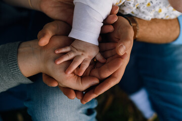 Hands of  mother and father are joined together, on top is the little plump hand of their baby. Love, warmth, care and protection are felt in touch.