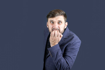 a bearded man in a blue suit bites his nails in fear