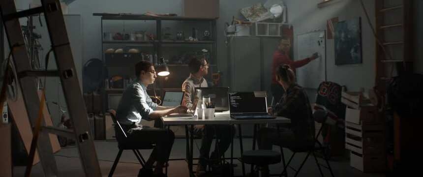 WIDE Group of young people discussing something, brainstorming. Launching their small IT business startup company from garage. Shot with 2x anamorphic lens