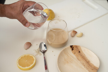 Tahini, lemon and garlic on the white table. How to cook tahini. First step for cooking. Glass of water and tahini. Tahini different from hummus. Traditional food. 
