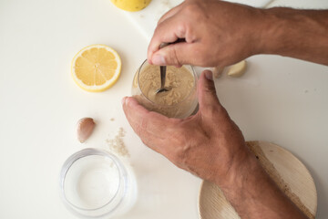 Tahini, lemon and garlic on the white table. How to cook tahini. First step for cooking. Glass of water and tahini. Tahini different from hummus. Traditional food.  