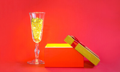 Open red gift box with golden glow and glitter inside and champagne glass with bubble beads, banner, copyspace. universal holiday, christmas, valentine's day, new year, birthday, anniversary, present