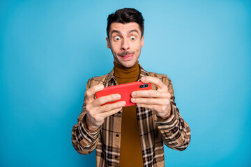 Photo of young funky funny focused addicted man playing video game in cellphone isolated on blue...