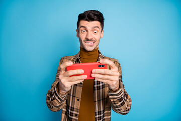 Photo of young happy crazy smiling addicted positive man playing video game in smartphone isolated on blue color background