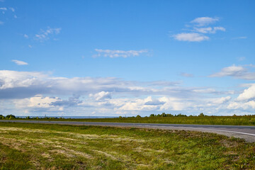Beautiful landscape with blue sky, white clouds and the road that goes to the horizon through field.