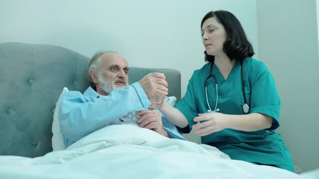 Caregiver bringing pills and glass of water to mature patient, elderly care