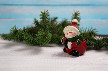 Christmas snowman toy stands on a white wooden board against the background of a blue wooden board with spruce branches