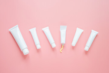 White cosmetic tubes on a pink background. Concept of face and body skin care, cosmetics. Top view, minimalism, flat lay, copy space.
