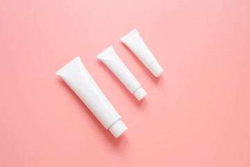 White cosmetic tubes on a pink background. Concept of face and body skin care, cosmetics. Top view, minimalism, flat lay, copy space.