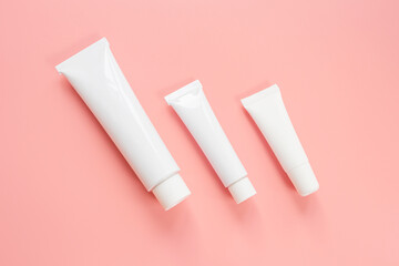 White cosmetic tubes on a pink background. Concept of face and body skin care, cosmetics. Top view, minimalism, flat lay, copy space.