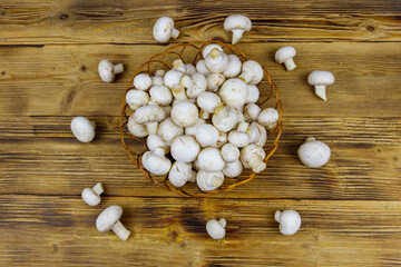 Fresh champignon mushrooms in wicker basket on the wooden table. Top view