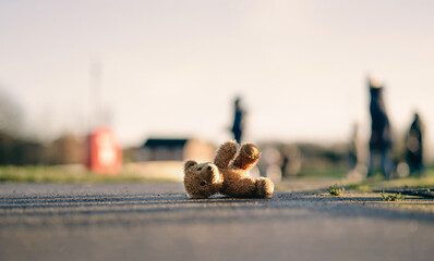 Lost Teddy bear with sad face lying on footpath with blurry people ,Lonely bear doll laying down on...