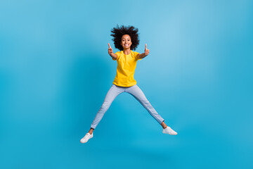 Fototapeta na wymiar Full body photo of brown haired dark skin little girl jump up show thumbs up wear casual outfit isolated on blue color background