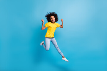 Full size photo of afro american trendy brunette little girl jump win wear yellow t-shirt jeans isolated on blue color background