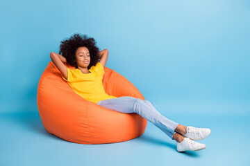 Full size photo of dark skin little brown haired girl sit sleep bean bag isolated on blue color...