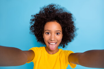 Photo funny dark skin brown haired little girl wear yellow t-shirt take selfie fooling face isolated on blue color background