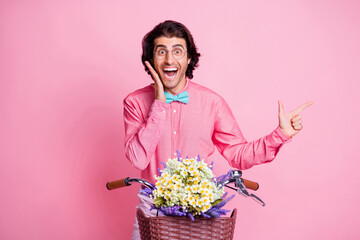 Photo of funny impressed brunet hair man spectacles sitting bike pointing empty space arm cheek...