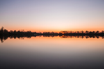 Landschaft und Sonnenuntergang mit Ufer des Sarchinger Weiher mit Spiegelung des Himmels in dem glatten See mit wunderschönen Farben Farbenspiel ohne Wolken, Deutschland
