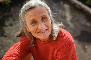 Close up portrait of a smiling senior woman with grey hair and face with wrinkles outdoors relaxing at park during sunny day