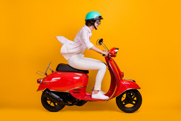 Side profile full length photo of pretty funky young girl riding motorbike enjoying highway trip wear white striped shirt pants helmet glasses isolated yellow vivid color background