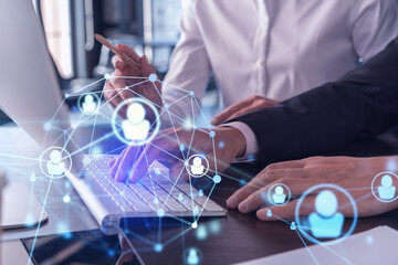 Two HR specialists in formal wear analyzing the recruitment market using laptop to boost the intern program at international consulting company. Social networking hologram icons.