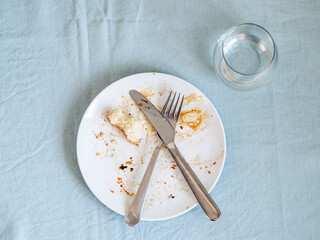 dirty plate after eating on the dining table. Top view of dirty white plate with crosswise cutlery...