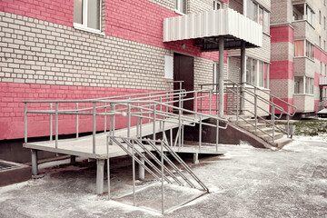 Ramp for baby strollers and wheelchairs with metal handrails at the entrance to the residential building