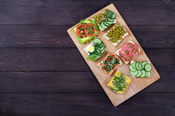 Fototapeta na wymiar Sandwiches on toast bread with cream cheese with salmon, sprouts, vegetables lie on a wooden board on a brown wooden background. Healthy food concept.