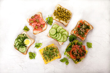 Various sandwiches with salted salmon, cucumbers, tomatoes, green peas, olives, sprouts on on white concrete background Healthy food concept.