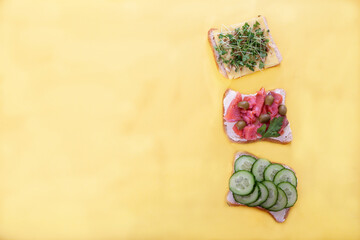 Various sandwiches with salted salmon, cucumbers, tomatoes, green peas, olives, sprouts on a yellow background. Healthy food concept.