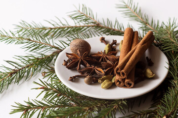 spices for mulled wine on a small white plate on a white background with green branches of a Christmas tree