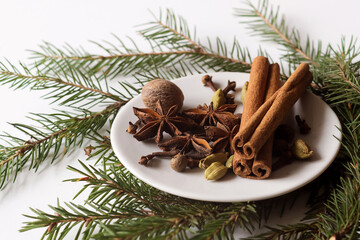 spices for mulled wine on a small white plate on a white background with green branches of a...