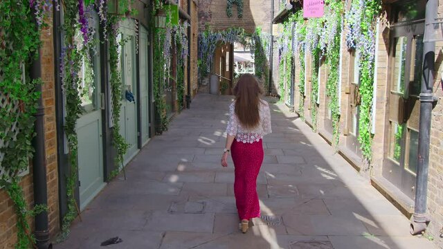 A fashionable in a red dress walking in slow-motion in the MayFair, London in 4K. Concept of a female walking down the restaurant streets of London, UK in the Mews of Mayfair.