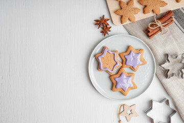 Portion of sweet savory gingerbread cookies with blue glaze served on gray plate on white wooden background with pastry cutters, textile towel and cinnamon. Image with copy space, flat lay