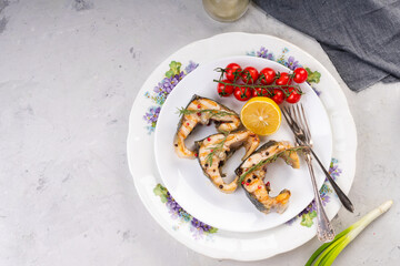 Grilled sturgeon steaks on a white plate with spices, cherry tomatoes and lemon. On a gray background.