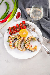 Fototapeta na wymiar Grilled sturgeon steaks on a white plate with spices, cherry tomatoes with a glass of wine. On a gray background.