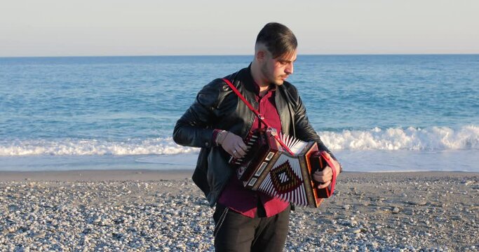 Ragazzo suona la tarantella calabrese con l'organetto in spiaggia vicino al mare