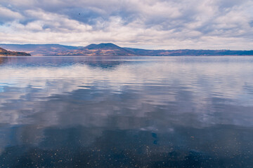 Obraz premium View of lake water reflecting a cloudy sky in a mountains landscape in Italy