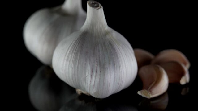 Close-up of organic two heads of garlic that lie on a table, isolated on a dark background. Next to it are garlic cloves.