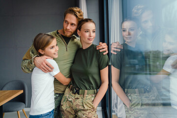 Beautiful happy family hugging while standing near window at home